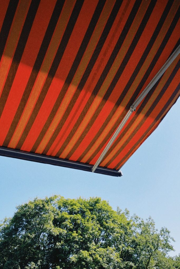 Colorful striped canopy in Belgium against bright sky and lush trees, dramatic composition.